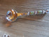 The Artisan Crafted Herb & Bath Salt Spoon Color Changing Mood Bead Scoop, with its vibrant patterns, silver accents, and decorative handle, rests on a wooden surface. Its round bowl shines beautifully, reflecting the surroundings.