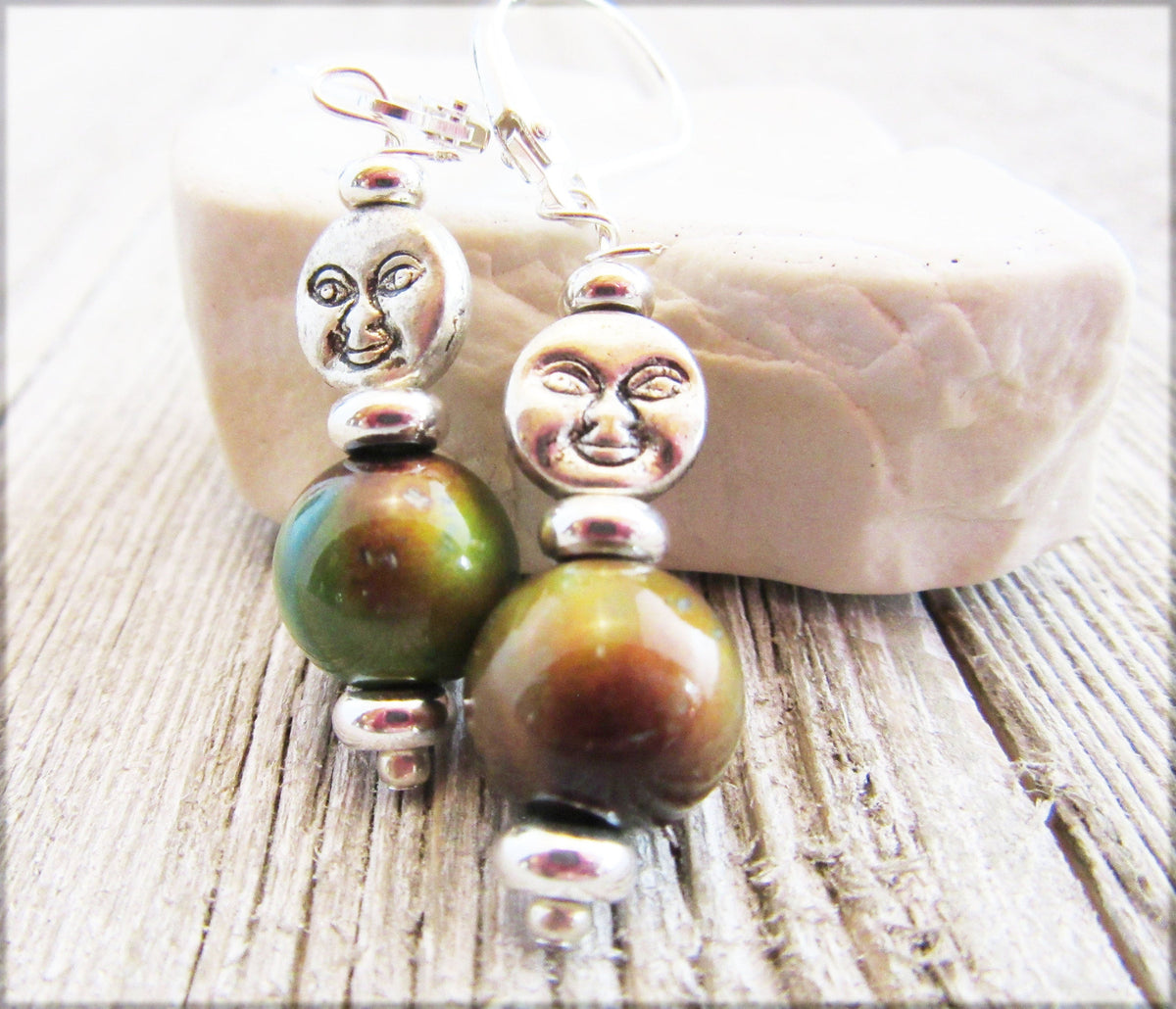 Spring Full Moon Silver Earrings with Color Changing Mood Beads showcase a lunar crescent moon face design and large green-brown mood beads, displayed on light wood with a white stone in the background.