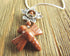 The Goldstone Dragonfly Necklace: Water Lily Pendant hangs from a silver chain and features a sparkling brown design, shown on a textured wooden surface.