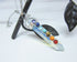 The Handcrafted Opalite Wand Pendant: Chakra Stone Necklace features seven colorful chakra stones on a silver chain, elegantly displayed over a black metal leaf—a distinctive piece of handmade jewelry.