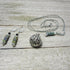 The Floral Diffuser Necklace Earring Set: Color Changing Aromatherapy Jewelry features intricate metalwork with floral designs in green and blue, displayed on a weathered wood surface. Includes dangling earrings and a filigree pendant necklace.