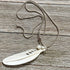 The White Feather Necklace features an angel sign carved bone and mother of pearl pendant, displayed on a rustic wooden surface—ideal for those seeking meaningful spiritual jewelry.