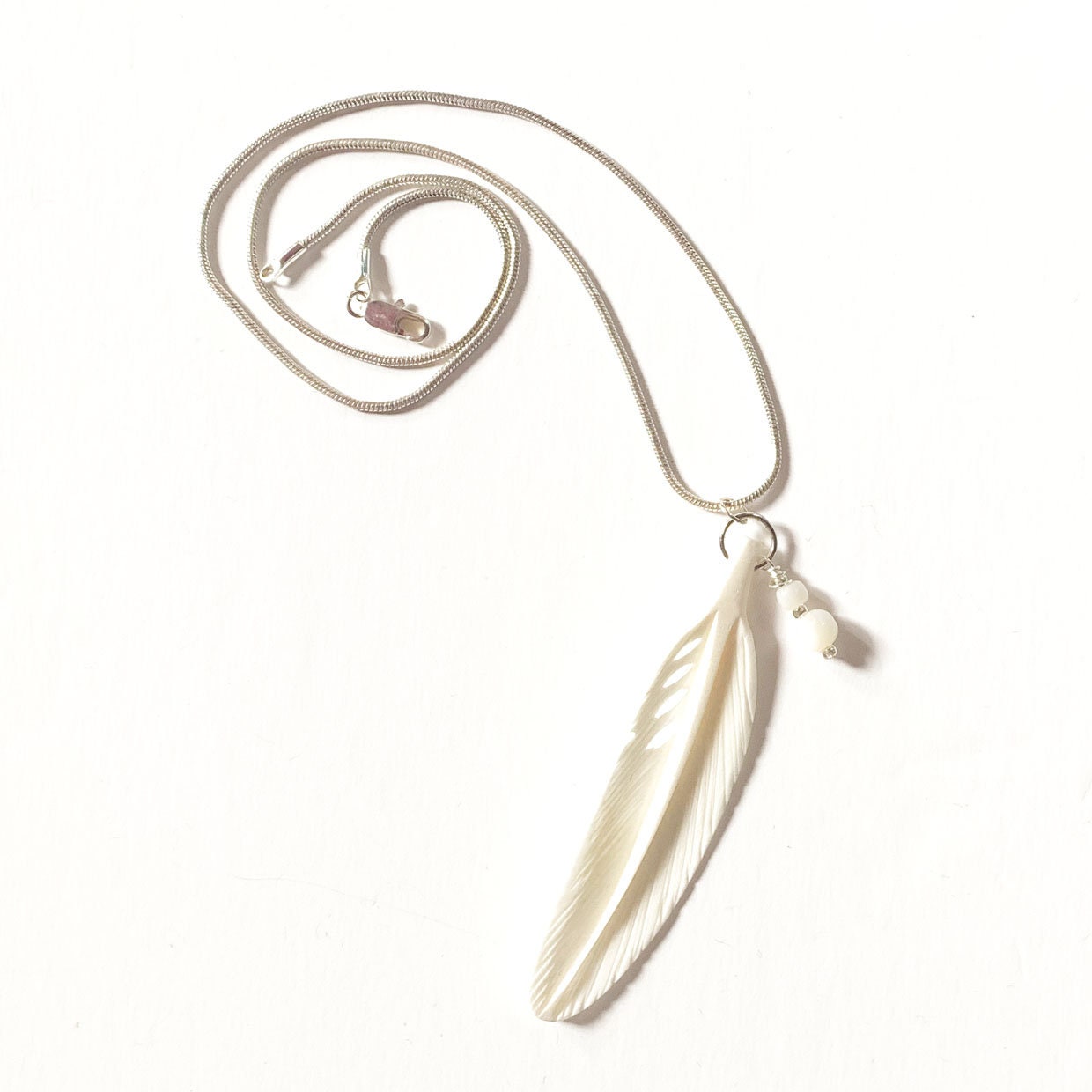 White Feather Necklace featuring a carved bone and mother of pearl pendant, symbolizing purity and strength, ideal for any outfit.