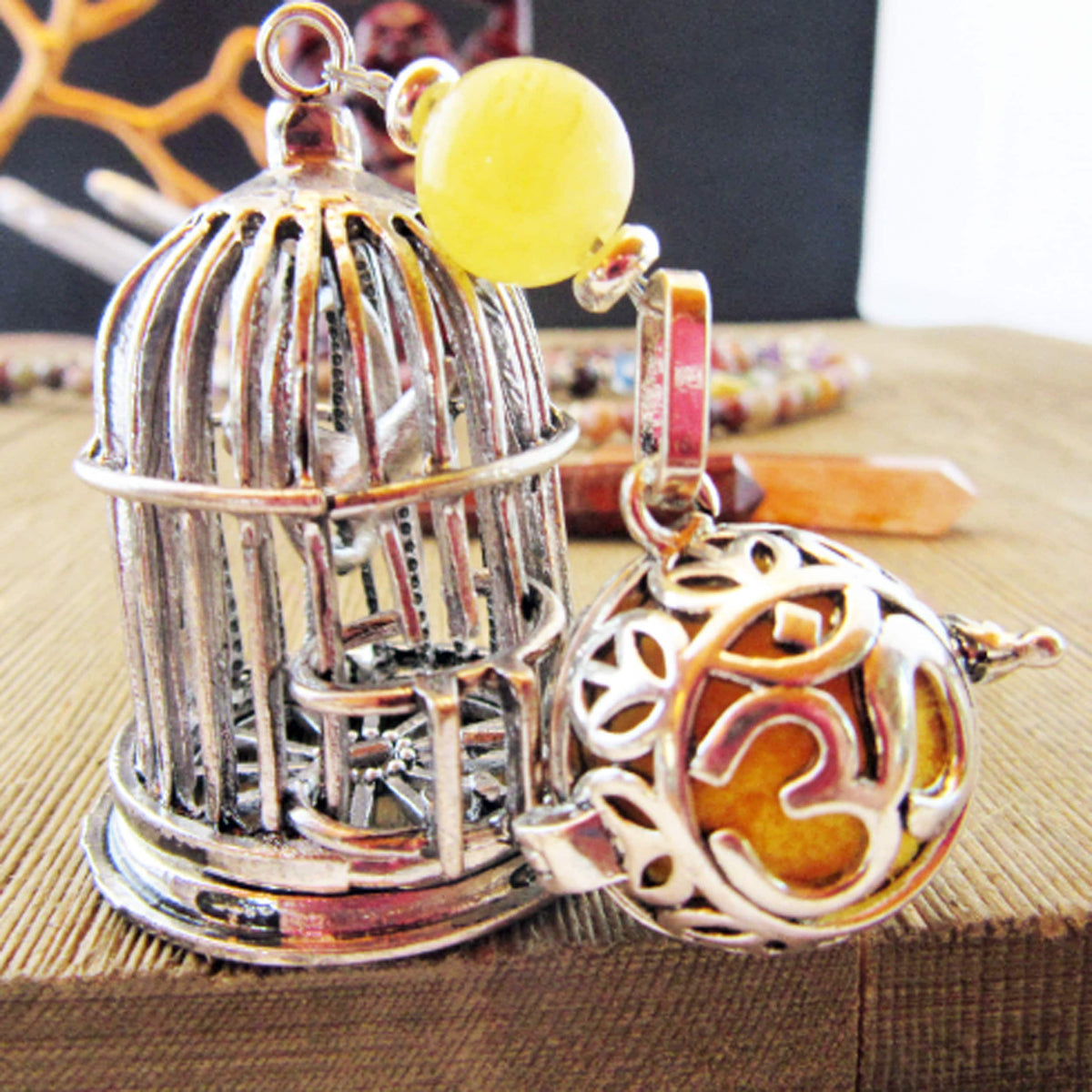 The Zen Bird Cage Essential Oil Diffuser features a decorative silver birdcage with a yellow calcite bead and lava bead locket etched with an Om symbol, perfect for aromatherapy and enjoying your favorite scents.