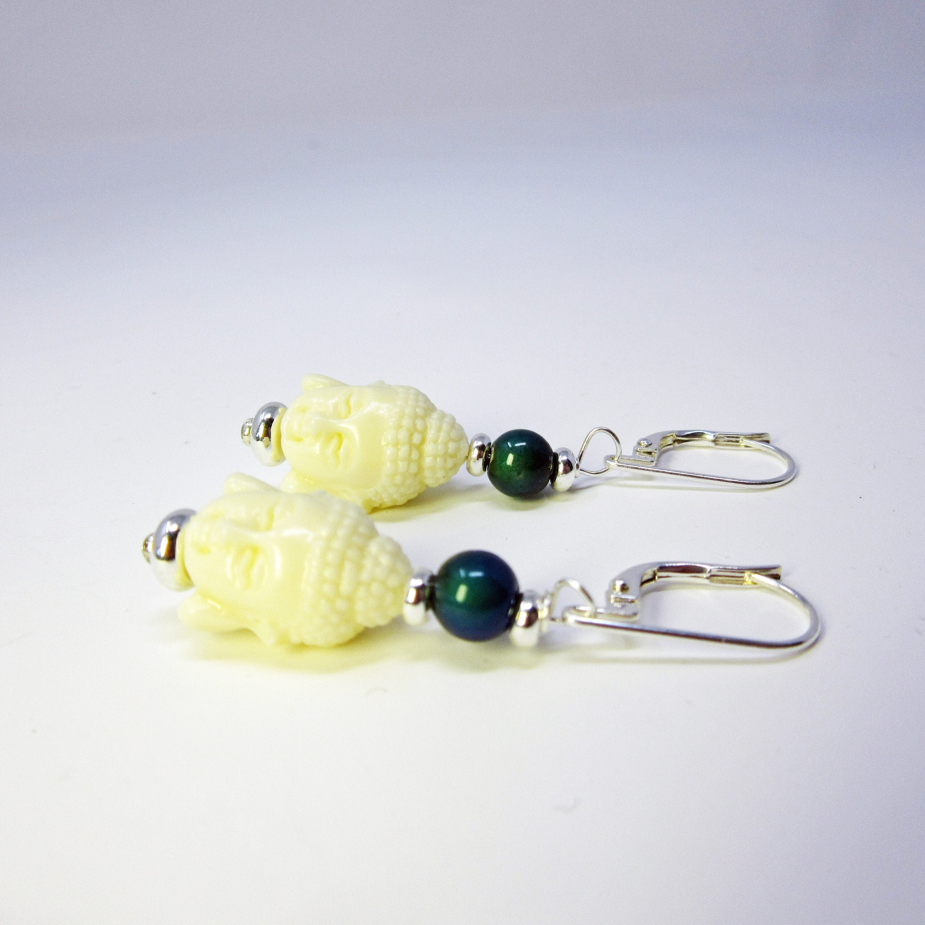 Kwan Yin Sterling Silver Earrings: Carved Stone Compassion Jewelry feature cream Buddha head charms, green round beads, and silver hooks, beautifully displayed on a white surface.
