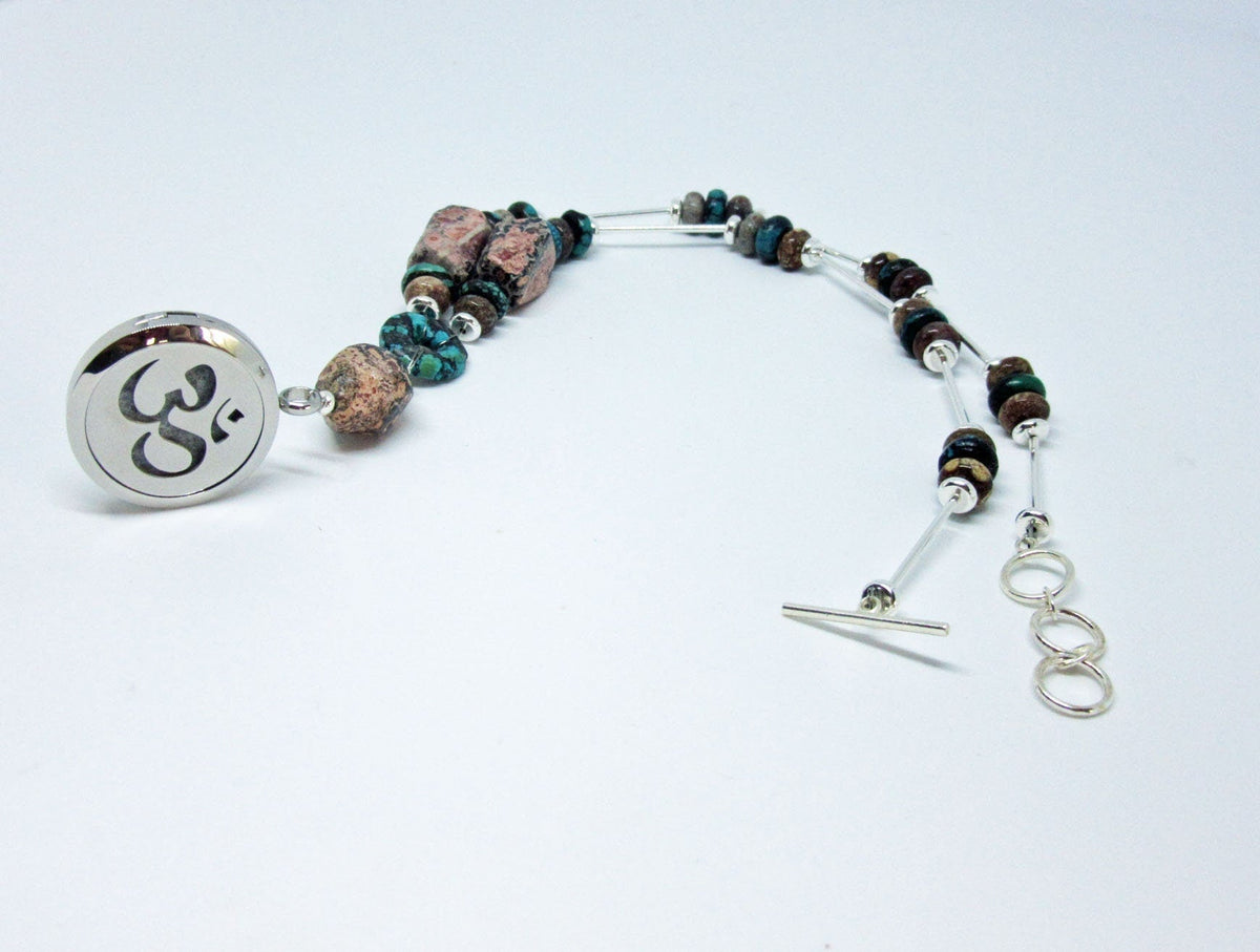 A beaded bracelet with mixed stones and silver accents plus a round charm engraved with the Om symbol, ideal for pairing with your Rhodochrosite Turquoise Essential Oil Diffuser Necklace or Silver Namaste Locket. Shown on a white background.