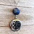 The Lapis Lazuli Aromatherapy Necklace & Sterling Silver Earrings set features a round lapis lazuli stone above an oval lotus locket, shown on a textured wooden background—a spiritual and elegant jewelry set.
