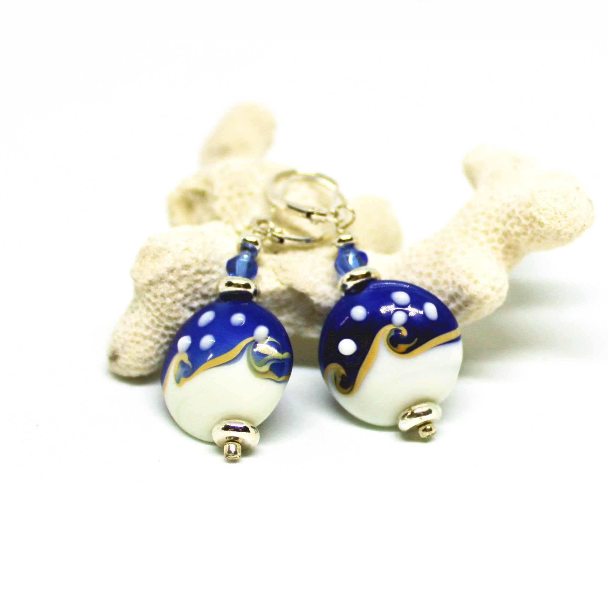 Ocean Wave Glass Earrings: Sterling Silver Nautical Dangles—featuring blue and white round glass with gold swirls and white dots, displayed before light coral on a white background for an elegant coastal look.
