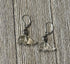 Manatee Earrings: Carved clear quartz charms with a decorative spiral hang from sterling silver lever backs, displayed on a wooden surface.