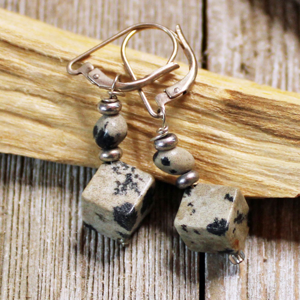 The Sacred Geometry Dalmatian Jasper Cube Earrings showcase beige cube stones with black speckles and silver hooks, highlighted by small silver beads—an ideal choice for Sterling Silver Artisan Jewelry lovers.