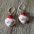 A pair of Lampwork Glass Heart Dangle Earrings—red and white lever back jewelry with heart-shaped beads—displayed on a wooden surface.