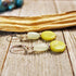 Aventurine & Quartz Hexagon Earrings—sterling silver with sacred geometry, featuring yellow-green and milky white stones, displayed on rustic wood beside driftwood.