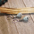Sesame Jasper Mint Earrings with Black Tourmaline in an artisan design and sterling silver hooks, featuring sacred geometry, are displayed on a wooden surface beside a palo santo stick.