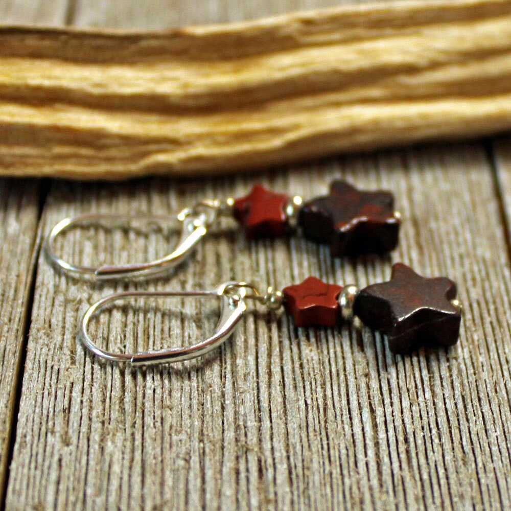 Star Dangle Earrings: Handmade sterling silver earrings with red and black gemstone star beads on silver hooks, displayed on rustic wood with dried plant material. Unique jewelry perfect as standout star dangle earrings.