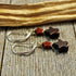 Star Dangle Earrings: Handmade sterling silver earrings with red and black gemstone star beads on silver hooks, displayed on rustic wood with dried plant material. Unique jewelry perfect as standout star dangle earrings.