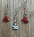 Two reddish-brown Carved Stone Animal Charms—one a Carnelian Rat, the other a Jasper Bunny Dangle—sit on string loops beside a grayish-white stone charm with dark patterns on a weathered wooden surface.