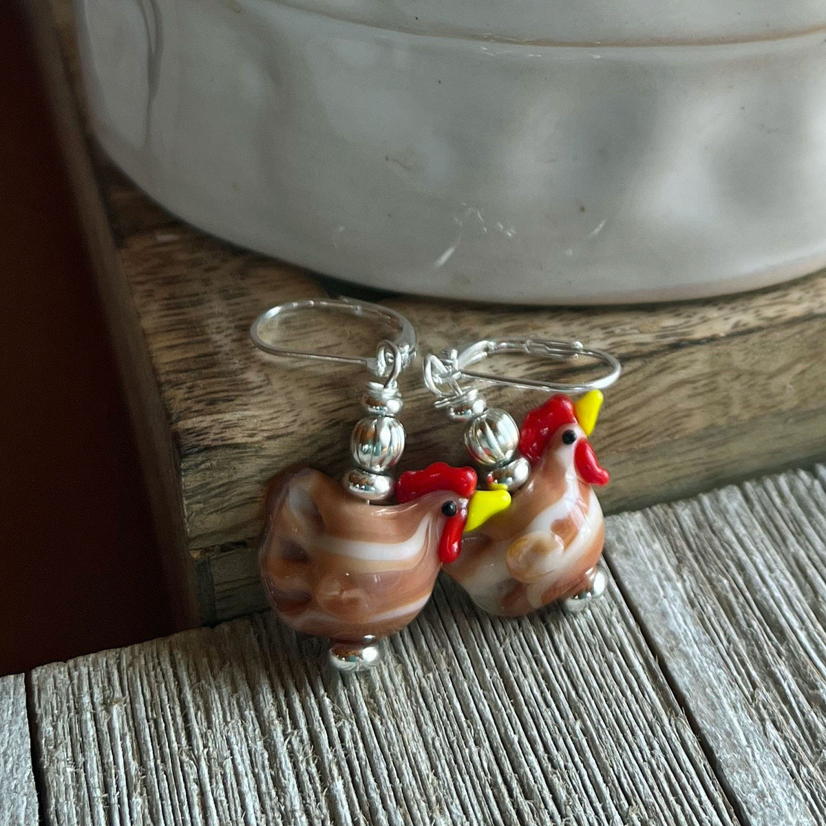 Close-up view of the unique white lamp work glass hen earrings - perfect gift for barnyard keepers.