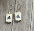 Mahjong Tile Earrings: Green Dragon Jewelry feature white rectangular tiles with green Chinese characters, metal hooks, and beige beads—displayed on rustic wood. A unique gift for any Mahjong player.