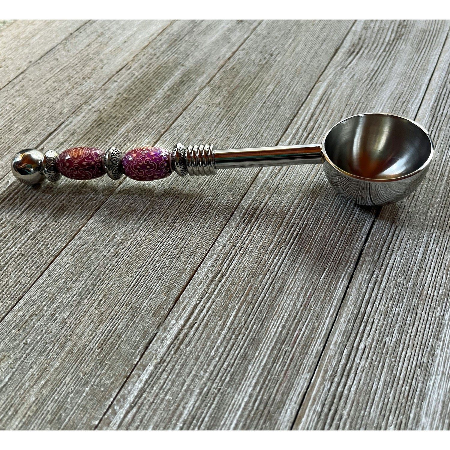 The Color-Changing Beaded Scoop: Herb, Bath Salt, Coffee Spoon—with purple and silver accents and an ornate handle—rests on a rustic wooden surface, making it a unique astrology gift or spiritual ritual tool.