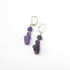 The Handcrafted Amethyst Goddess Earrings: Willendorf Venus Jewelry feature silver hooks with dangling purple gemstone beads, each uniquely shaped, adding artisanal charm and elegance to any outfit.