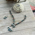 The Artisan Designed Fancy Jasper Jewelry Set with a sterling silver peacock clasp features a beaded necklace and matching earrings in green, brown, and blue tones, beautifully displayed on wood with sea-inspired accents.