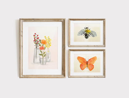 A trio of watercolor paintings printed on textural watercolor paper. The left image of glass vases with red, orange, and yellow flowers with Dreams painted on one glass. The top shows a watercolor bee and the bottom is a bright orange butterfly
