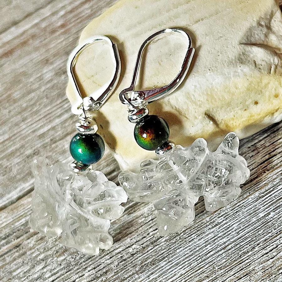 The Clear Dragon Earrings are handmade fantasy jewelry featuring color-changing quartz, iridescent dark green beads, and sterling silver hooks, displayed on rustic wood with a light rock in the background.