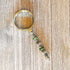 The Daisy Green Beaded Magnifier, a handmade silver office crafting tool with green accents, rests on a wooden surface displaying its unique beaded handle and elegant design.