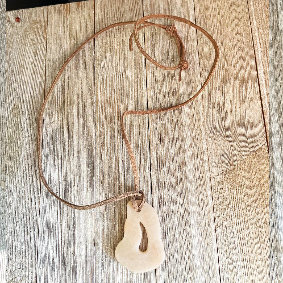 The Adjustable Leather Necklace with Stone Pendant: Minimalist Earthy Jewelry features a natural, uniquely shaped stone on an adjustable leather cord, presented on rustic wood—a striking piece of minimalist style.