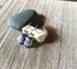 Handcrafted Glass Owl Earrings with color change topper beads and blue-white patterns are displayed on stacked stones atop a rustic wooden surface.