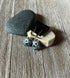Enchanting Handcrafted Animal-Themed Owl Earrings with blue and white details are displayed on a black stand atop smooth stones—unique whimsical woodland jewelry, perfect as a bird lover gift.