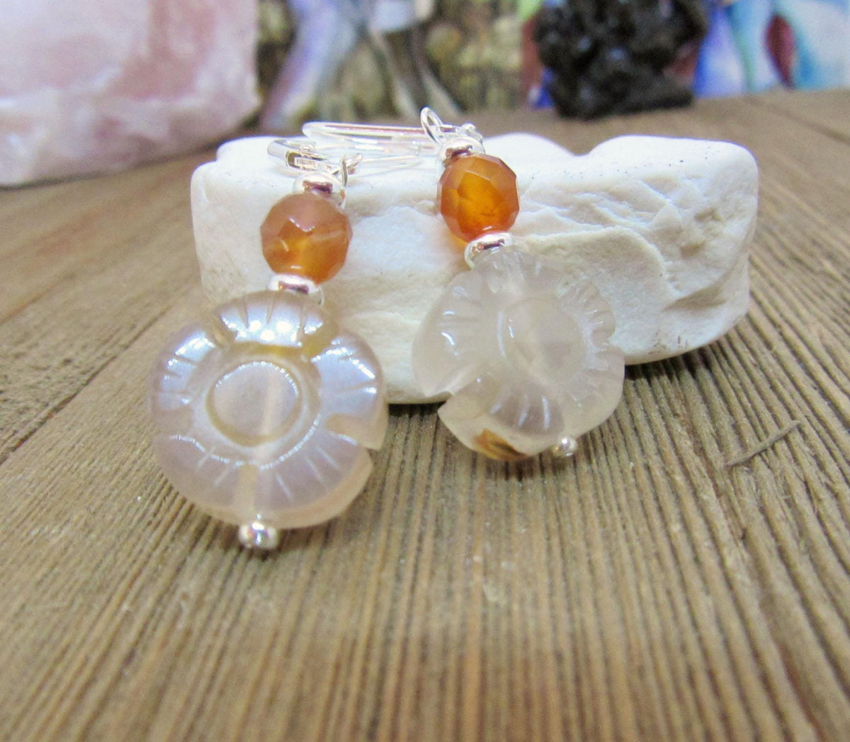 A pair of Sunflower Earrings for Spring—cream and carnelian agate flower dangle earrings in a handmade boho style, displayed on textured white stone with a wooden surface background.