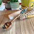The Zodiac Coffee Scoop – Beaded Handle, Zen Herb Spoon for Earth signs (Virgo, Capricorn, Taurus) rests on a wooden surface with sage, selenite crystal, plants, and a yellow mug in the background.