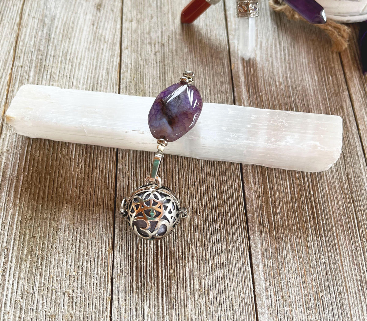 The Handcrafted Zen Aromatherapy Chamber features a large purple agate stone and a round, detailed Namaste symbol, presented on a white crystal base atop a wooden surface.