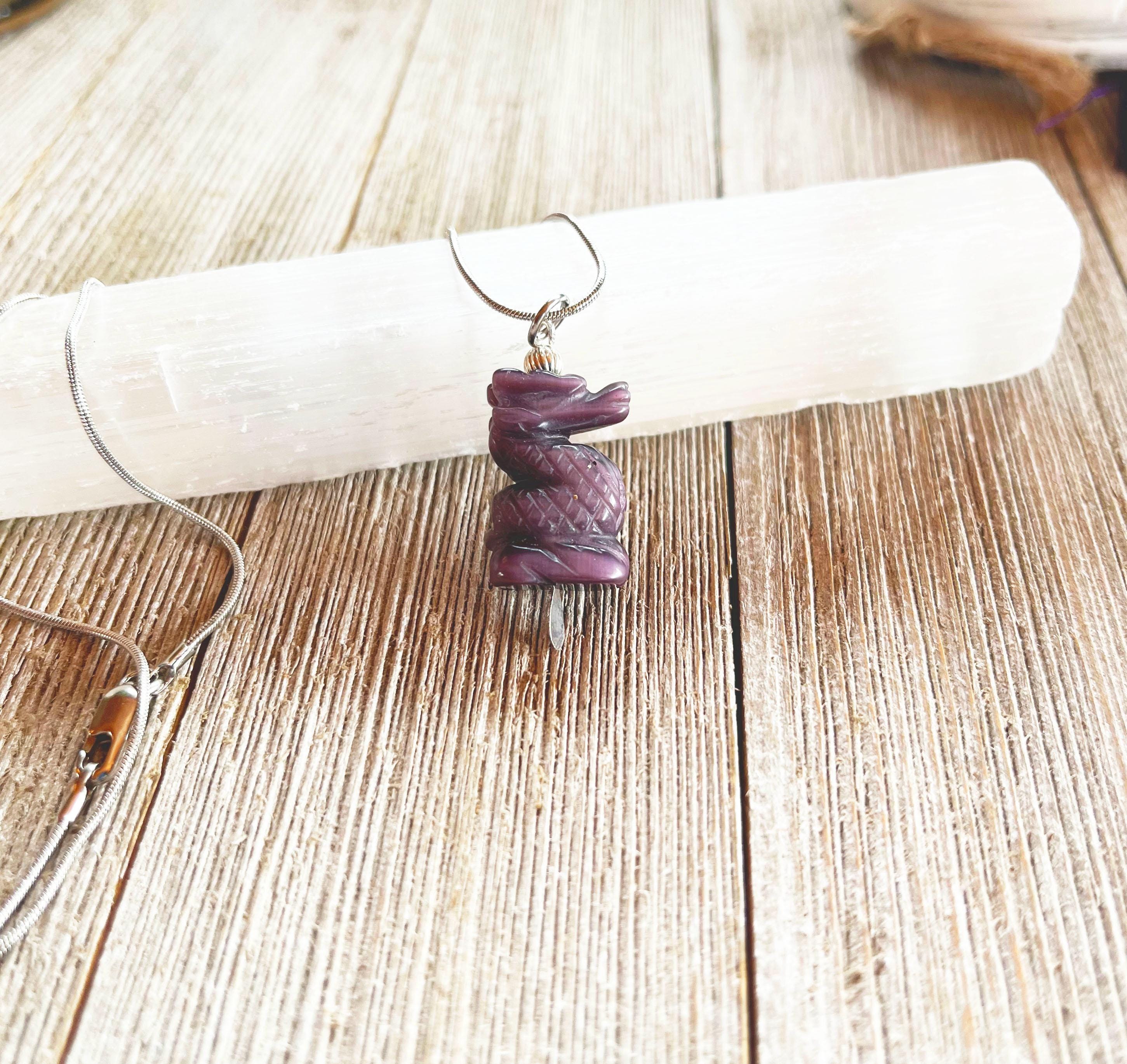 The Purple Dragon Pendant Necklace: Fantasy Glass Jewelry features a spiral-carved purple stone on a silver chain, displayed atop a white crystal wand on a rustic wooden surface.