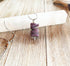 The Purple Dragon Pendant Necklace: Fantasy Glass Jewelry features a spiral-carved purple stone on a silver chain, displayed atop a white crystal wand on a rustic wooden surface.