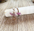 Turtle Earrings Amethyst Carved with Silver Swirl Detail are shown hanging on a white crystal atop a rustic wooden surface—a beautiful, nature-inspired jewelry piece for animal lovers.