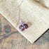 The Bunny Rabbit Necklace features a playful hare pendant and a round amethyst-like lavender bead, beautifully displayed on burlap fabric over rustic wood—an ideal jewelry gift for amethyst lovers.