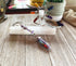 A decorative wand with gemstone beads and a crystal tip rests on selenite atop wood, paired with a crystal chakra decor, potted plant, and the Chakra Amethyst Metal Bookmark—a Zen Gift for Book Lovers.