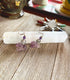 A pair of Horse Earrings Pony Equestrian Jewelry Handcrafted Carved Stone with silver spiral accents and purple stones rest on a white crystal wand atop wood, with colorful crystals and a cup in the background.