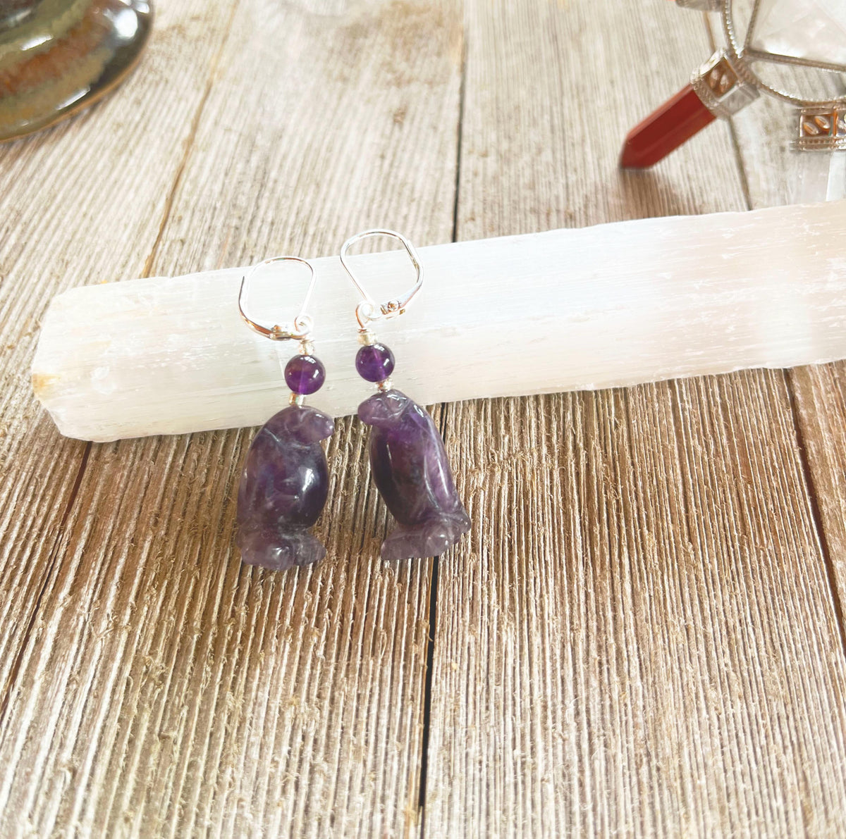 Purple Amethyst Penguin Earrings—featuring bear-shaped pendants and round beads, displayed on a white selenite wand on rustic wood. These playful earrings are perfect animal lover jewelry for any nature enthusiast.