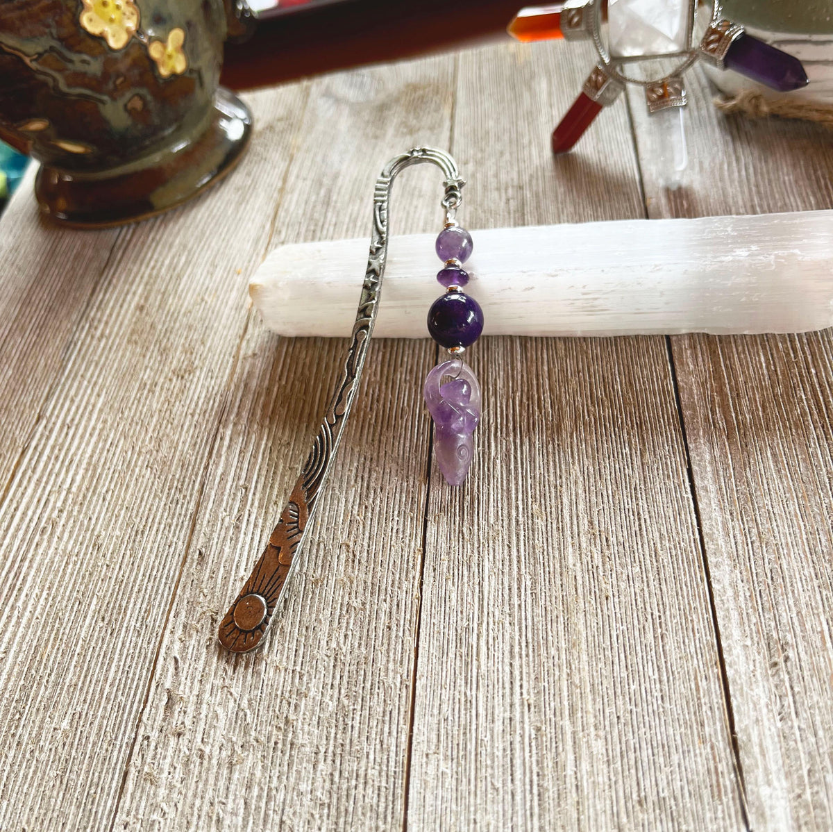 The Amethyst Bookmark: Artisan Designed Divine Goddess Celestial Gift features engraved metal, purple beads, and an amethyst angel charm, pictured on a white selenite stick—making it a perfect celestial-themed present.
