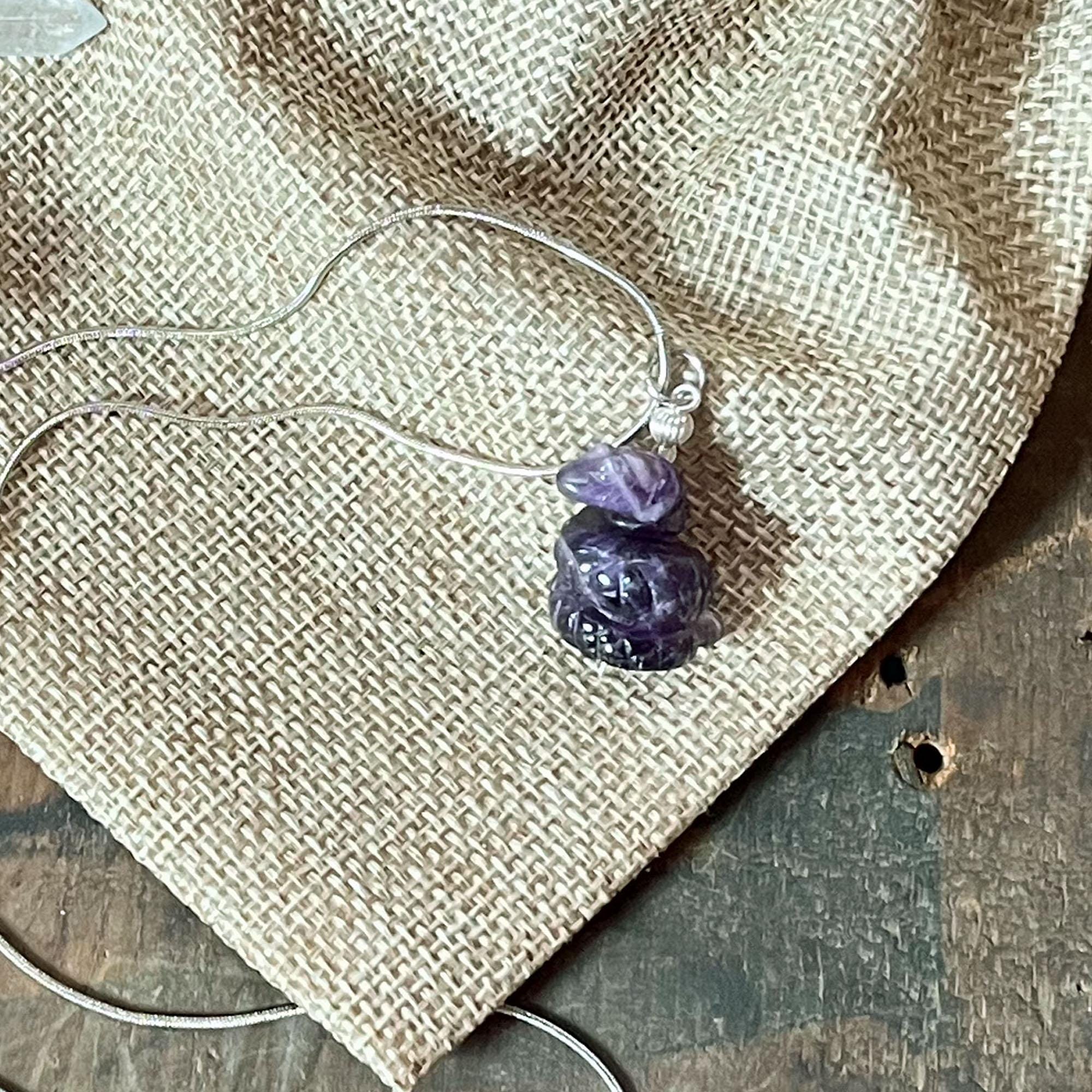 The Serpent Pendant Necklace—handcrafted with wire-wrapped amethyst in a spiritual snake design—rests on textured burlap fabric, with part of a wooden surface visible in the background.