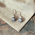 Sterling Silver Teapot Earrings feature round lavender jasper stones and whimsical design, displayed on burlap fabric over a wooden surface.