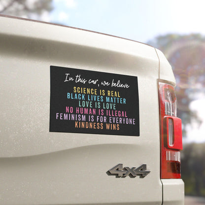 Black car bumper magnet with distressed block lettering that reads: “In this car, we believe: science is real, black lives matter, love is love, no human is illegal, feminism is for everyone, and kindness wins.”