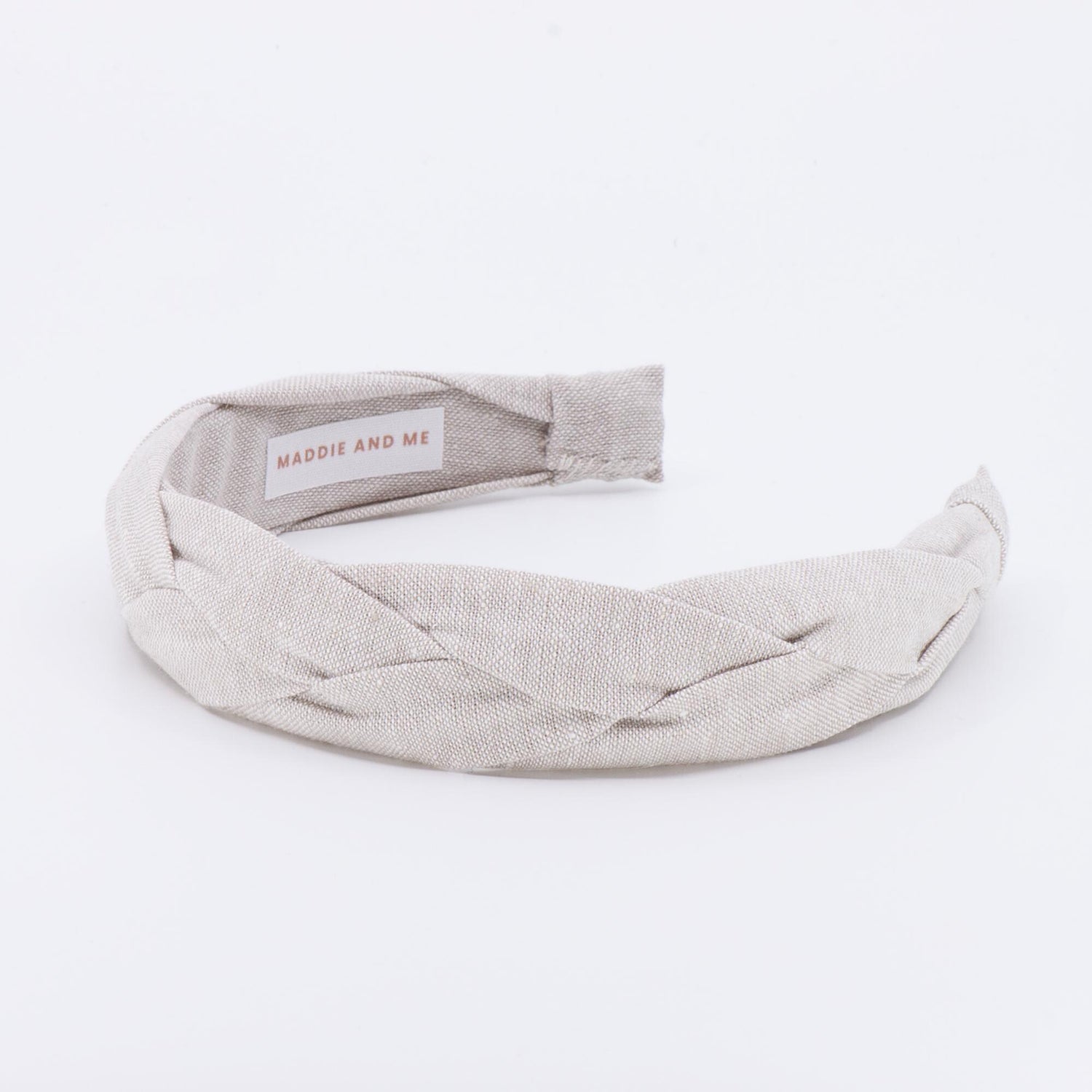A light tan braided linen headband. The headband has a label that says &amp;quot;MADDIE AND ME&amp;quot;.