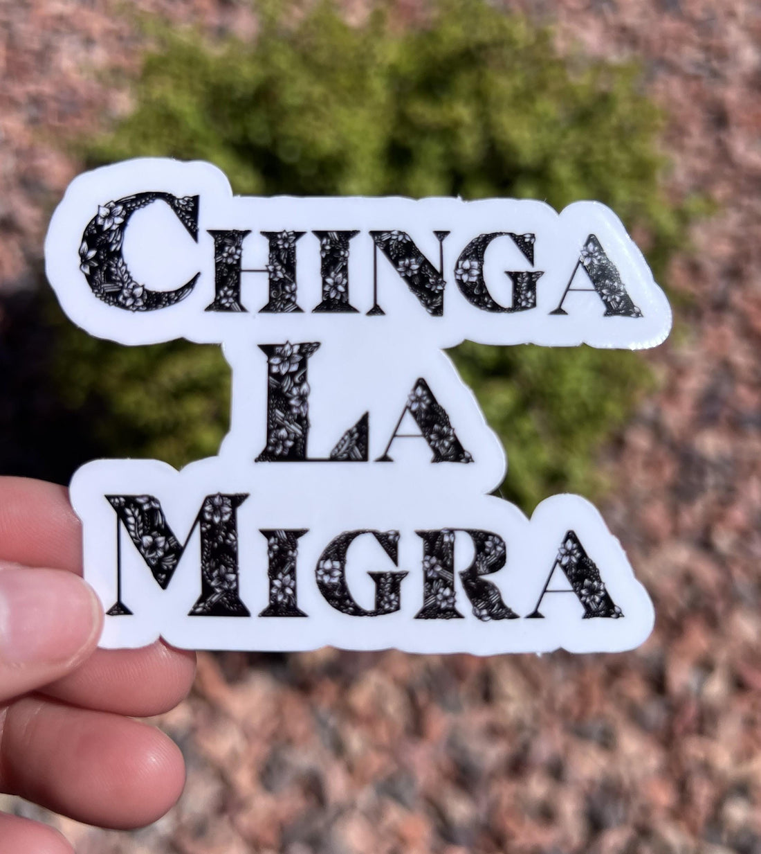 May include: A white sticker with the words &amp;quot;CHINGA LA MIGRA&amp;quot; in black, floral-patterned letters.