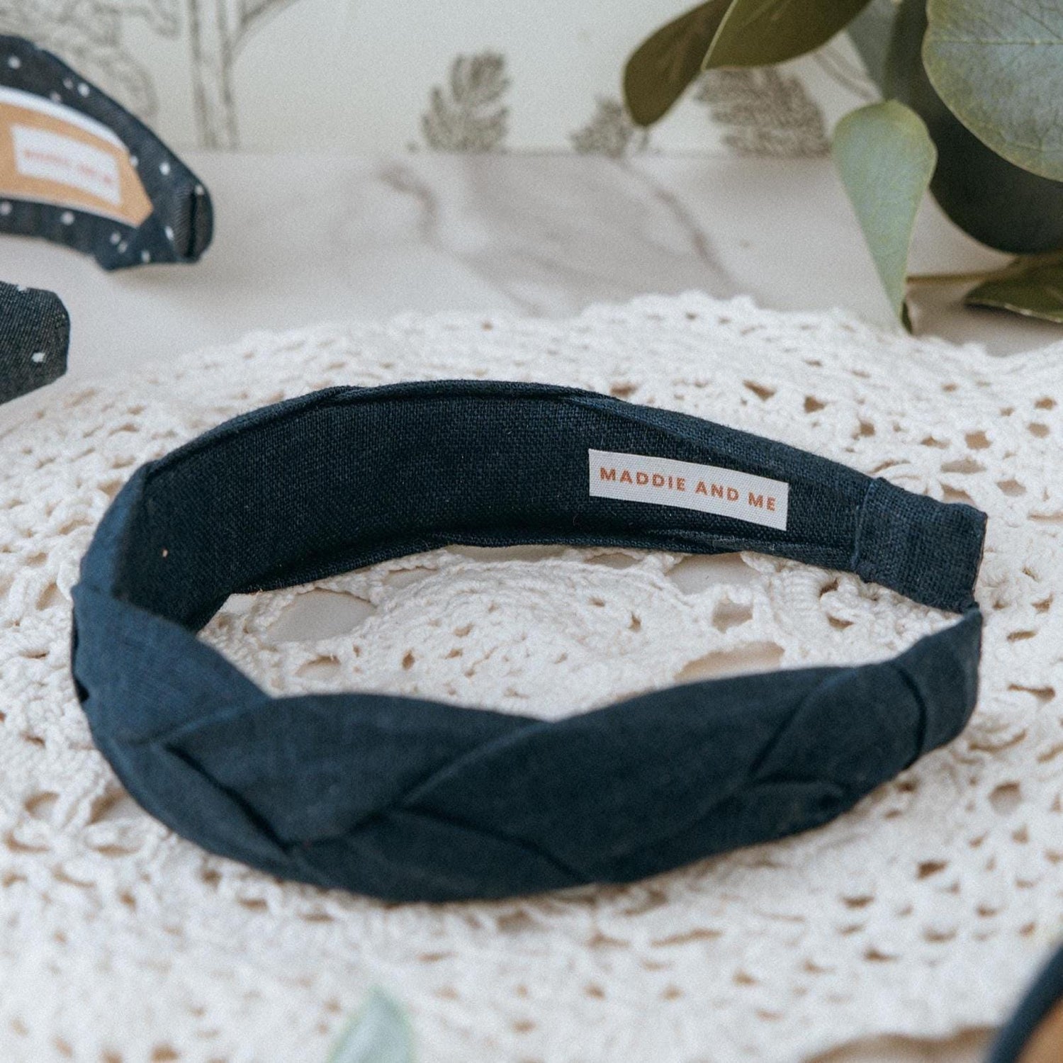 May include: A dark navy blue braided headband made of linen fabric. The headband has a label that says &amp;quot;MADDIE AND ME&amp;quot;.
