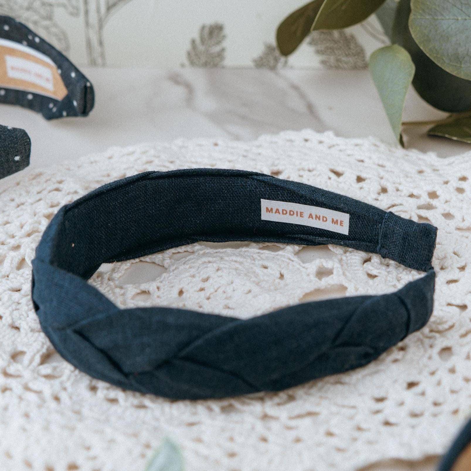 May include: A dark navy blue braided headband made of linen fabric. The headband has a label that says &amp;quot;MADDIE AND ME&amp;quot;.