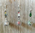 Three Crystal Christmas Tree Ornament - Scent Locket Holiday Decorations hang against a wood backdrop, each featuring a beaded Christmas tree in yellow, red, or green above an ornate silver sphere.
